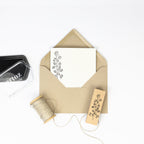 Abgebildet ist ein brauner Umschlag mit einer Karte im Artoz Papier AG Stempel Beerenzweig Design, einer Garnrolle, einem passenden Holzstempel und einem schwarzen Stempelkissen - ideal für Ihre nächsten Bastelarbeiten auf weißem Hintergrund.