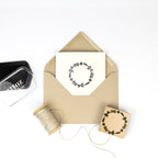 Une enveloppe brune contient une carte avec un motif floral noir Stempel Kranz d'Artoz Papier AG, présenté à côté d'une ficelle, d'un tampon encreur et du tampon assorti - idéal pour les travaux créatifs de Bastelarbeiten sur fond blanc.