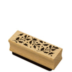 L'Artoz Papier AG Stempel Stechpalme est un tampon rectangulaire en bois avec des feuilles de houx noires et des baies sur le dessus - idéal pour les Bastelarbeiten ou les Einladungskarten festives. Présenté de biais sur fond blanc.