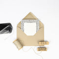 Une enveloppe en papier kraft contenant une carte décorative est entourée des éléments essentiels de Bastelarbeiten : de la ficelle, un tampon encreur noir et deux Artoz Papier AG Stempel Stechpalme, dont l'un est estampillé "HO HO HO", le tout présenté sur un fond blanc.