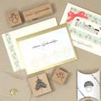 Ein Flat Lay mit weihnachtlichen Bastelarbeiten und Schreibwaren mit dem "Stempel rote Beeren" der Artoz Papier AG, festlichen Karten mit deutschem Text, einem Umschlag mit Wachssiegel und einer Geschenkschachtel mit einer Pilzillustration.