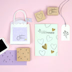 Eine flache Lage von österlichen Bastelarbeiten auf rosa, die das Artoz Papier AG Stempel Frohe Ostern Set mit Geschenktüte, Herz- und Blumenholzstempel, Stempelkissen, "öffnen UND FREUEN!"-Karte mit Herzen und einem floralen Geschenkanhänger zeigt - ideal für Frohe Ostern!.