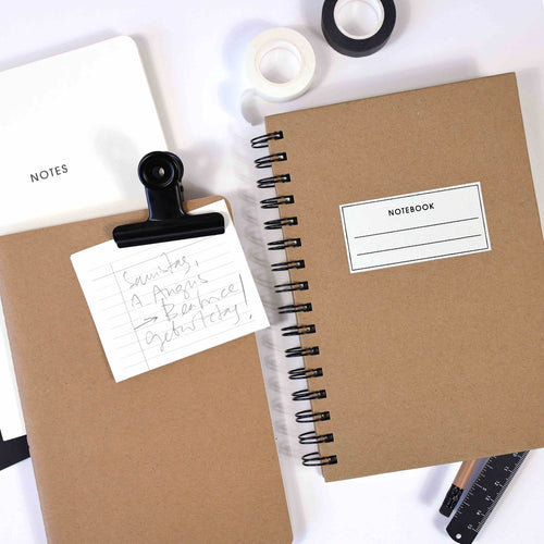 Deux carnets de notes A5 bruns d'Artoz Papier AG - l'un à reliure spirale, l'autre à couverture rigide avec clip et note manuscrite - sont présentés sur une surface blanche avec une règle, du washi tape noir et blanc et un carnet de notes blanc "NOTES". Parfait pour l'écriture en ligne.