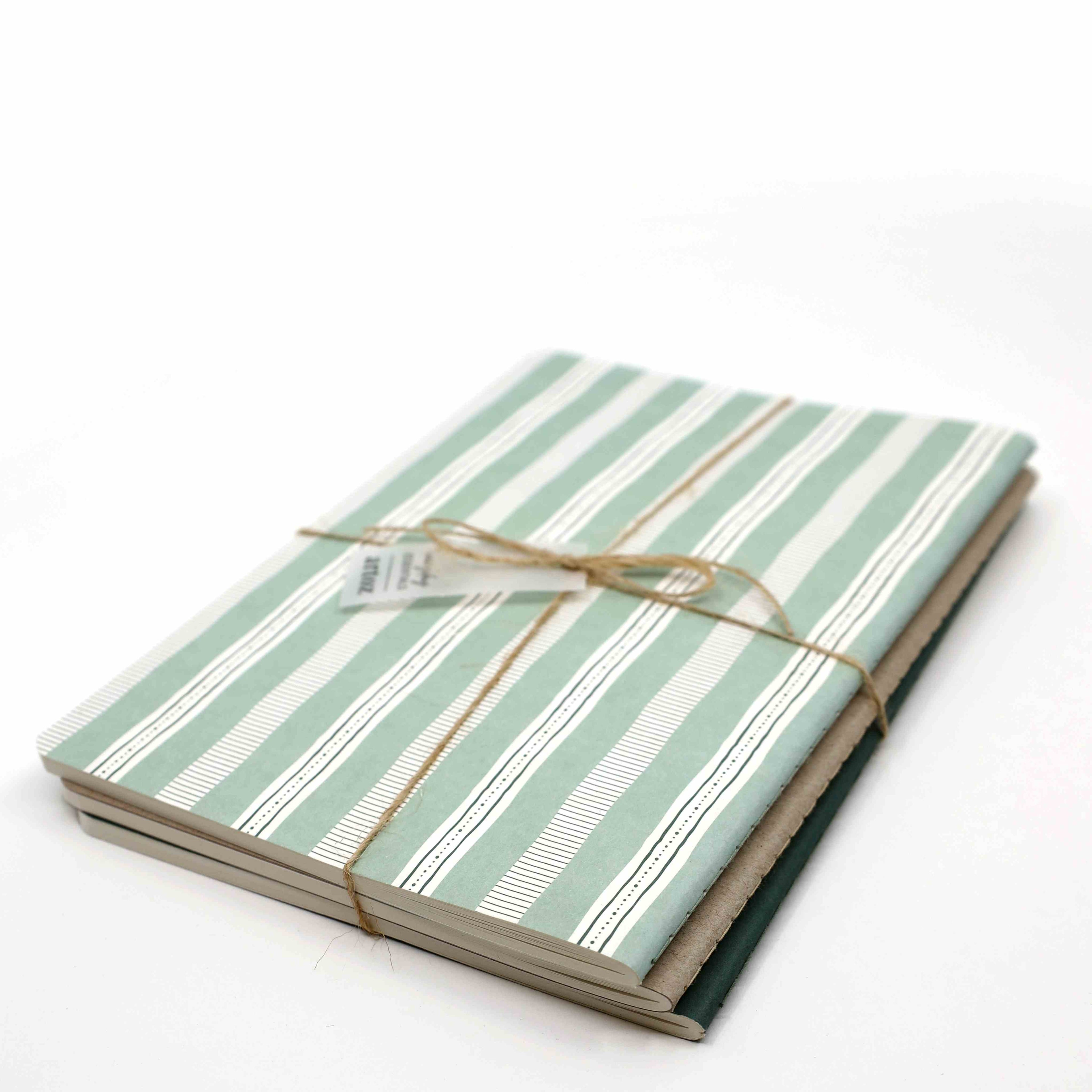 Le A5 Notizheft 3er Set farbig d'Artoz Papier AG comprend trois carnets A5 à pois avec des couvertures rayées vertes et blanches, attachées avec de la ficelle marron. Chaque carnet est fabriqué sur un papier de qualité supérieure de 80 g/m² et se détache sur un fond blanc uni.