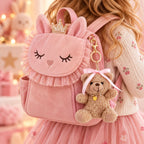 Une petite fille vêtue d'un tutu rose et d'un pull à fleurs porte un sac à dos rose en forme de lapin, orné du pendentif « Teddy » – ours en peluche avec un nœud dans les cheveux – de la marque Artoz Papier AG et surmonté d'une couronne. L'arrière-plan aux couleurs pastel, baigné d'une lumière douce, met en valeur cette scène pleine de charme, ce qui en fait une idée de cadeau idéale pour les tout-petits qui adorent l'élégance ludique.