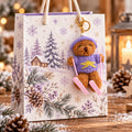 Eine festliche Geschenktüte zeigt eine bezaubernde Winterhütten-Szene, geschmückt mit Tannenzapfen und Schneeflocken. Als entzückendes Accessoire hängt am Henkel der Tüte der „Ski-Teddy“-Anhänger von Artoz Papier AG – ein kleines Plüschbärchen, das einen lila Pullover und eine Mütze trägt und mit rosa Skiern ausgestattet ist. Kerzen und Tannenzapfen im Hintergrund runden dieses perfekte Geschenkzubehör für Ihre Weihnachtsfeiern ab.