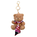Der „Teddy Anhänger – Plüschbär mit Halstuch“ von Artoz Papier AG ist ein brauner Plüsch-Teddybär als Schlüsselanhänger mit goldenem Verschluss und Ring, der mit einem rot-weiß-schwarz-rosa gestreiften Schal verziert ist – und damit das perfekte, niedliche Wintergeschenk ist.