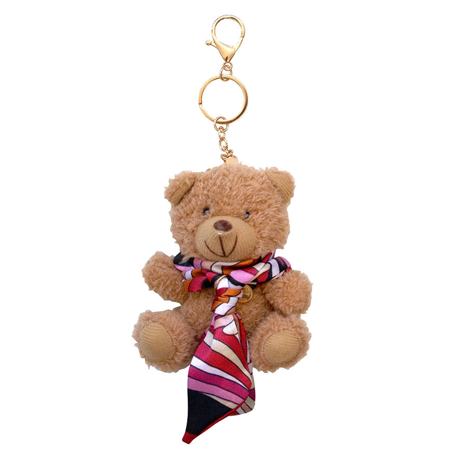 Der „Teddy Anhänger – Plüschbär mit Halstuch“ von Artoz Papier AG ist ein brauner Plüsch-Teddybär als Schlüsselanhänger mit goldenem Verschluss und Ring, der mit einem rot-weiß-schwarz-rosa gestreiften Schal verziert ist – und damit das perfekte, niedliche Wintergeschenk ist.