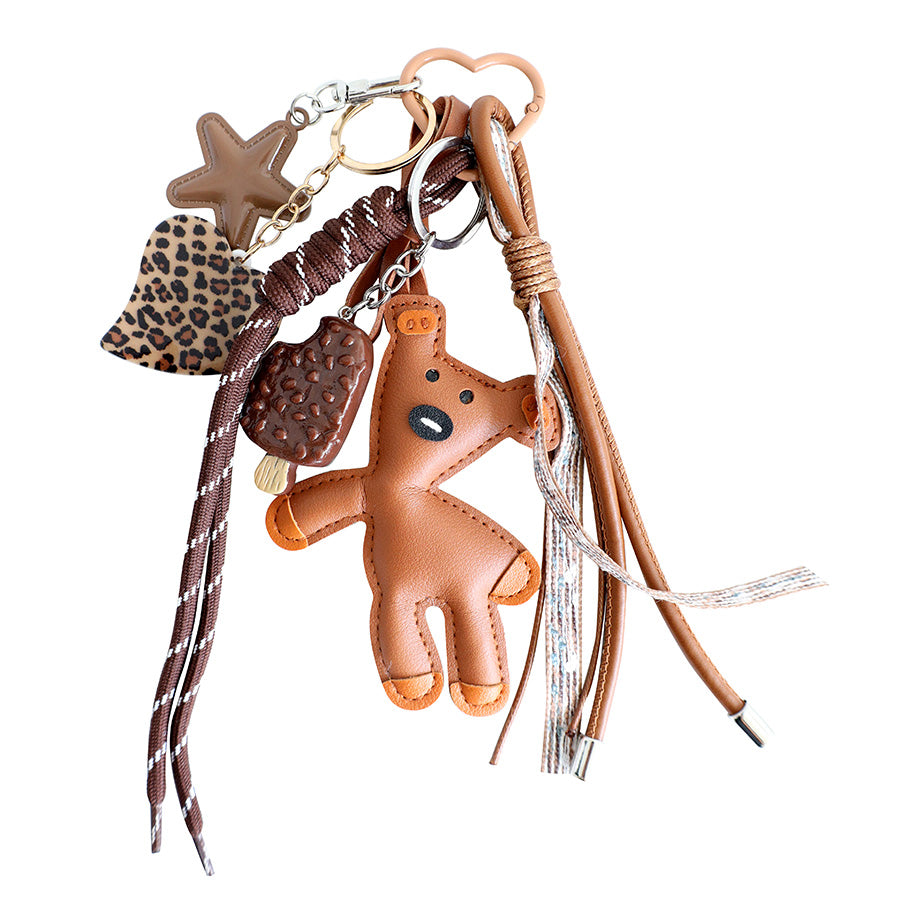 Le pendentif « Teddybär » en PU aspect cuir d'Artoz Papier AG se compose d'un ours brun aspect cuir, d'un cœur à imprimé léopard, d'une étoile, d'un pendentif en forme de tablette de chocolat, de cordons tressés et de pompons en cuir, ce qui en fait une charmante idée de cadeau pour tous ceux qui aiment les accessoires originaux.