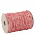 Une bobine de Artoz Papier AG Geschenkband Rot, d'une longueur de 20 mètres et d'un éclat métallique subtil, fabriquée à partir d'un mélange de jute et de polyester et enroulée proprement autour d'une bobine en carton, est présentée sur un fond blanc.