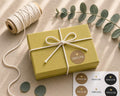 Une boîte-cadeau « Pure S » rectangulaire de la marque Artoz Papier AG, de couleur verte, fermée par une ficelle blanche et ornée d’un autocollant doré en forme de cœur portant l’inscription « Dankeschön », repose sur un support beige aux côtés d’une bobine de ficelle, de feuilles d’eucalyptus et d’autres autocollants « Dankeschön ». La structure en carton de la boîte garantit sa solidité et permet de la réutiliser pour de futures occasions de cadeaux.