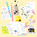 Une mise en page à plat de l'Inhaltset für Tischbomben - Thema "Kids Party" d'Artoz Papier AG : cartes de jeu, pièces de morpion, pailles en papier, confettis, tatouages, bouteilles de peinture, gommes à effacer et cartes sur fond jaune. Parfait comme Nachfüllset !.