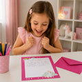 Ein kleines Mädchen in einem rosa Kleid strahlt beim Anblick eines handgeschriebenen Briefes auf Briefpapier aus dem „Einhorn“-Schreibset für Kinder der Artoz Papier AG; im Hintergrund sind Buntstifte, ein rosa Umschlag und Einhorn-Verzierungen aus dem Set zu sehen.