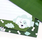 Gros plan sur le coffret de papier à lettres Kinder « Hund » de la marque Artoz Papier AG, de couleur verte, orné d'un adorable chien blanc, d'os et de nuages sur les bords. Certaines feuilles de ce coffret de papier à lettres pour enfants sont lignées et soigneusement empilées.