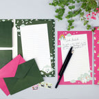 Eine Flat-Lay-Aufnahme von zwei geöffneten Schreibmappen des „Einhorn“-Schreibsets für Kinder von Artoz Papier AG mit niedlichen Tiermotiven, Briefpapier, Stiften, rosa und grünen Briefumschlägen, Briefmarken und Topfpflanzen vor einem hellgrauen Hintergrund.