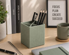 Le porte-stylos Artoz Papier AG, de couleur verte, vous permet de ranger vos stylos et crayons noirs sur un bureau en bois, à côté d'une tasse à café, d'un cahier, de plantes et de livres : un équipement de bureau à domicile idéal pour vous aider à VOUS CONCENTRER, PLANIFIER, CRÉER ET RÉUSSIR.