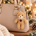 Eine beige Handtasche, verziert mit dem Artoz Papier AG Teddy-Anhänger – Plüschbär mit Herzkette, der eine Perlenkette und einen braunen Herzanhänger trägt, liegt auf einer Holzunterlage, umgeben von festlicher Winterdekoration – und ist damit das perfekte Wintergeschenk.