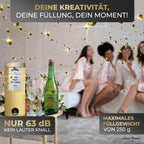 Die kinderfreundliche Tischbombe ohne Feuer "DIY" 5er Set von Artoz Papier AG steht auf dem Tisch mit zwei Sektgläsern und Flasche; vier Frauen in pinken Bademänteln lachen im Hintergrund.