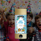 Quatre enfants coiffés de chapeaux de fête font la fête avec des confettis. Sur le devant, une bombe de fête Artoz Papier AG Tischbombe ohne Feuer - Happy Birthday Boy, avec des motifs d'animaux amusants et un texte en allemand, apporte un peu plus de piment à toute fête d'anniversaire.
