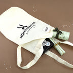 Un sac cadeau en tissu de couleur crème, orné du motif « Petit merci » de la marque Artoz Papier AG, contient trois cadeaux emballés et une étiquette portant le nom « Nia », le tout posé sur un fond marron parsemé de petits points décoratifs blancs : un emballage écologique idéal pour tout cadeau de remerciement.