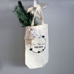 Un sac-cadeau en tissu de couleur crème, orné du motif « Von Herzen für Dich » de la marque Artoz Papier AG et décoré de cœurs noirs, est suspendu à un crochet. Un petit rameau de pin, une décoration blanche et une étiquette portant l'inscription « Danke » sont fixés au sac, ce qui en fait un emballage charmant et écologique pour votre cadeau spécial.