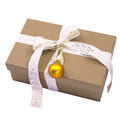 Une Geschenk-Box Pure M rect. grocer kraft by Artoz Papier AG, marron et nouée avec un ruban blanc "HO HO HO", décorée d'un petit ornement de Noël doré.