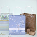 Das Geschenktaschen-Set "Gans" der Artoz Papier AG enthält drei Geschenktaschen: blau gestreift mit Schmetterlingsschleife, blaues Entenmuster mit Windrädchen-Dekor und braun mit weißen Herzen - sowie einen Hasenstempel, einen weiteren Stempel und Konfetti.