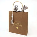 Le set Artoz Papier AG Geschenktaschen-Set Happy Birthday (198) se compose d'un sac cadeau en papier kraft marron avec la mention "Happy Birthday", un cœur doré, un pompon, des perles sur la poignée et un décor en eucalyptus - idéal comme Papiergeschenktüten pour les grandes occasions.