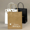 Le set de vaisselle "Herzensmensch" d'Artoz Papier AG comprend trois vaisselles : Le jaune avec des motifs dorés, le papier kraft avec la mention "Herzens-Mensch" et Herzmotiv, et le noir avec des motifs dorés - disposés sur un fond neutre.