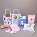 Le set Artoz Papier AG Geschenktaschen-Set Blumen (182) présente des sacs cadeaux, des boîtes et des enveloppes de couleur pastel avec des motifs floraux, des étiquettes, des cœurs et des pompons, disposés sur une surface gris clair avec un arrière-plan assorti.