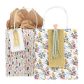 Le coffret Artoz Papier AG Geschenktaschen-Set (131) comprend deux sacs cadeaux colorés aux motifs floraux et abstraits : l'un avec un tissu marron et une étiquette "happy day", l'autre orné d'un ruban bleu, d'un cœur rose et d'une étiquette décorative.