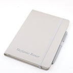 Un carnet A5 beige à couvercle fermé avec stylo, de la marque Artoz Papier AG, personnalisé au nom de Stefanie Riner sur la couverture, fermé par un élastique et muni d'un stylo à bille beige assorti fixé sur le côté.