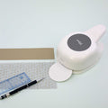 L'Artoz Papier AG Stanzer L Kreis (70 mm) est placé à côté d'une bande de papier brun, d'une règle claire, d'un stylo noir et d'une feuille avec des formes grises - des fournitures idéales pour les projets Basteln sur une surface blanche.