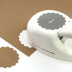 La perforatrice Artoz Papier AG Stanzer L Wellen-Kreis (Blütenmotiv, 76 mm) permet de découper des cercles festonnés dans du papier brun et blanc - idéal pour les projets créatifs.