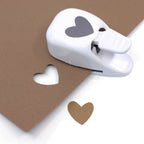 Une feuille blanche Artoz Papier AG Stanzer S Herz asymétrique est posée sur une feuille marron avec une découpe en forme de cœur, idéale pour le scrapbooking ou la création de cœurs en papier marron assortis.