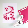 Sur une feuille blanche figure un grand chiffre 2 composé de papillons rouges et roses superposés. À proximité se trouvent Artoz Papier AG Stanzer S Schmetterling et un carré magenta avec des découpes de papillons - idéal Bastelzubehör for Karten gestalten.