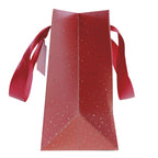 Une vue de profil du sac cadeau « Pure M Weihnachtlich » de la société Artoz Papier AG, dans des tons festifs de rouge et d'or, orné de pois dorés et de larges poignées en ruban rouge sur fond blanc.