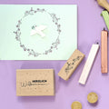 Une carte de vœux avec une colombe blanche et une couronne de fleurs repose sur un fond violet, entourée de Stempel Blumenzweig d'Artoz Papier AG, de bâtons de cire à cacheter et de sceaux de cire - parfaits pour le Bastelarbeiten. Sur l'un des timbres, on peut lire "Herzlich Willkommen.