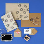 Les motifs d'Artoz Papier AG Stempel Kussmund décorent des cartes de vœux et des enveloppes sur une surface bleue. Une carte circulaire porte l'inscription "Miss. Katrin Maier I'm hot & cool bird" avec des empreintes de lèvres, ainsi qu'un tampon encreur Holzstempel.