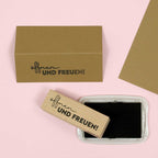 Le timbre "Öffnen und Freuen" d'Artoz Papier AG, accompagné d'un timbre-poste assorti et d'un tampon encreur noir, repose sur une surface rose - idéal pour les travaux de construction ou la création d'Einladungskarten créatifs.