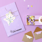 Une mise en page plate de papier à lettres sur le thème du violet d'Artoz Papier AG : enveloppe florale avec ficelle, enveloppes à motifs bruns, confettis, et le sceau "Öffnen und Freuen" - idéal pour Bastelarbeiten ou pour créer des Einladungskarten uniques sur un fond lavande.