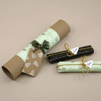Eine braune Papierrolle mit grüner Verpackung, verziert mit einer Schleife und einem baumförmigen Anhänger, der mit dem Stempel „Tannenbaum klein“ von Artoz Papier AG gestaltet wurde, liegt neben zwei Geschenken, die mit den Namen „Lila“ und „Tim“ beschriftet und mit goldenen Schnurschleifen verziert sind – alles auf einer beigen Unterlage arrangiert: die perfekte Inspiration für DIY-Bastelprojekte mit wunderschönen Akzenten, die mit dem Stempel „Holz“ gestaltet wurden.