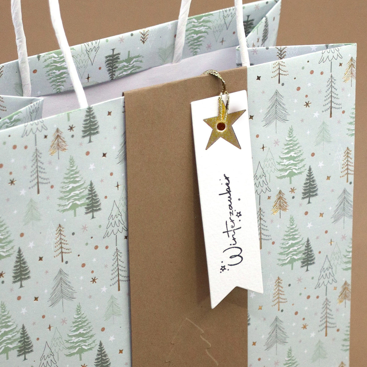 Ce sac cadeau proposé par Artoz Papier AG, orné d'un motif de sapin d'hiver (Tannenbaum Motiv) avec une bande marron et une étiquette blanche décorée d'une étoile dorée portant l'inscription « Winterzauber », est parfait pour rehausser vos projets de scrapbooking ou vous inspirer pour votre prochaine création « Stempel Winterzauber ».