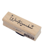 Un tampon rectangulaire « Winterzauber » de la marque Artoz Papier AG, sur lequel figurent le mot « Winterzauber » et de petites illustrations d'étoiles en haut. Orné d'un charmant motif de sapin de Noël, ce tampon en hêtre (Holzstempel Buche) est idéal pour les projets de scrapbooking. Sur le côté figurent un code-barres et les dimensions.