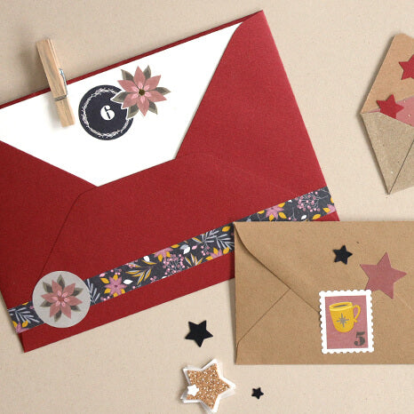 Ein roter Umschlag mit Blumenmuster und ein brauner Umschlag, verziert mit Stern- und Tassen-Aufklebern – darunter die „Artoz Sticker Adventsnummern 1–24 schwarz“ von Artoz Papier AG – sind auf einer beigen Unterlage angeordnet und von schwarzen und goldenen Sternausschnitten umgeben – ideal zum Dekorieren von Geschenken.