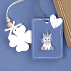 La présentation à plat montre une étiquette cadeau blanche en forme de trèfle avec des perles en bois et un nœud, un autocollant Artoz 3D Sticker "Einhorn" blau by Artoz Papier AG, et une enveloppe marron décorée d'un accent en papier en forme de cœur.