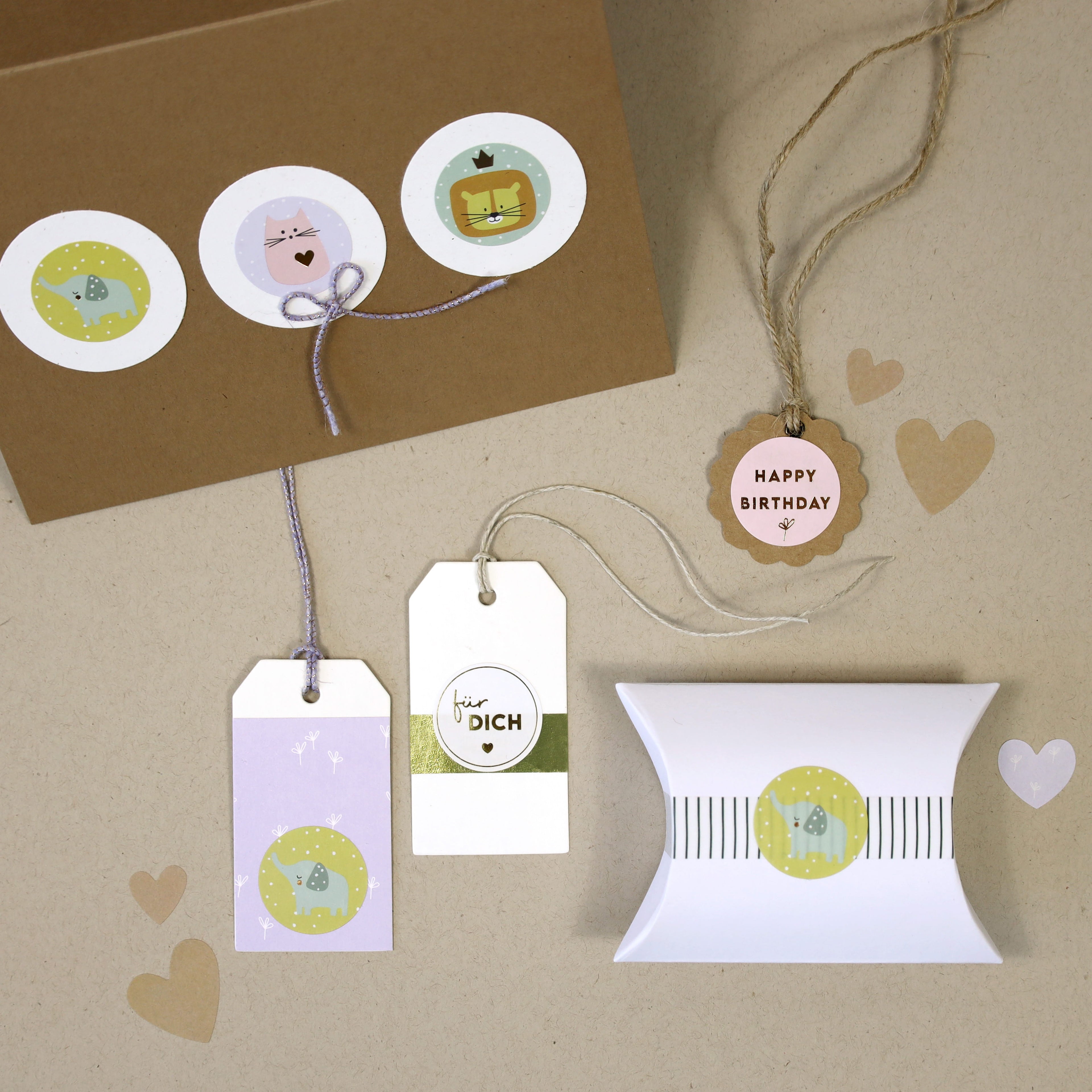 Eine Auswahl von Artoz Sticker für DICH von Artoz Papier AG auf beigem Hintergrund, mit pastellfarbenen Geschenkanhängern mit Tiermotiven und Sprüchen wie für DICH und HAPPY BIRTHDAY - einige mit Schnur gebunden, einer auf einer weißen Geschenkbox.