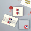 Une mise à plat de trois cadeaux d'anniversaire emballés, deux avec des étiquettes Happy Birthday et de petites bougies, décorés avec Bastelzubehör et Artoz 3D Sticker "Kerzen Happy Birthday" par Artoz Papier AG, entourés de cœurs et de cercles en papier sur fond gris.