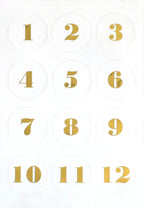 Douze cercles blancs comportant les chiffres dorés de 1 à 12, disposés en grille 3x4 sur fond blanc — parfaits pour les projets d'Avent ou comme matériel de loisirs créatifs, grâce aux autocollants transparents « Artoz Sticker Advent » d'Artoz Papier AG.