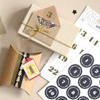Des coffrets cadeaux ornés d’étiquettes décoratives et de dentelle sont posés à côté d’une feuille d’autocollants transparents « Artoz Sticker Advent » d’Artoz Papier AG, parfaits pour réaliser un calendrier de l’Avent. L'une des boîtes est agrémentée d'une ficelle dorée et d'une enveloppe, tandis que l'autre est ornée d'une étiquette festonnée, d'un ruban et d'un autocollant de l'Avent transparent d'Artoz Papier AG, apportant ainsi une touche parfaite à vos projets créatifs.